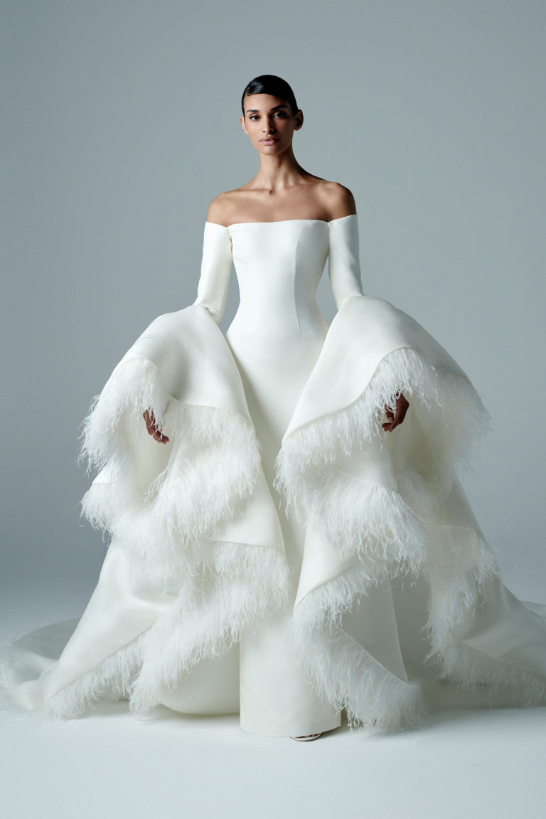 Off the shoulder tubino wedding dress with dramatic bell sleeves decorated with feathers